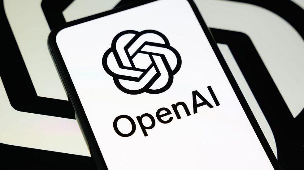 OpenAI's logo in black and white on a phone against a black and white spiral backdrop like its logo