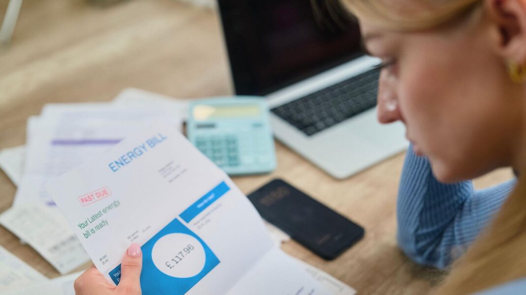 Woman looks at energy bill with paperwork, a calculator and a laptop on the table in front of her.