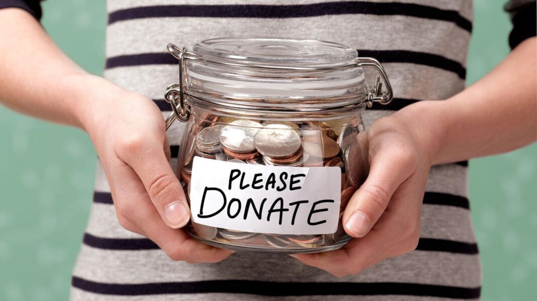 How much should you give to the office whip-round? A shot of someone's torso, in a black and white striped top, holding a glass jar with coins in it. On the front is a label that reads: Please donate.