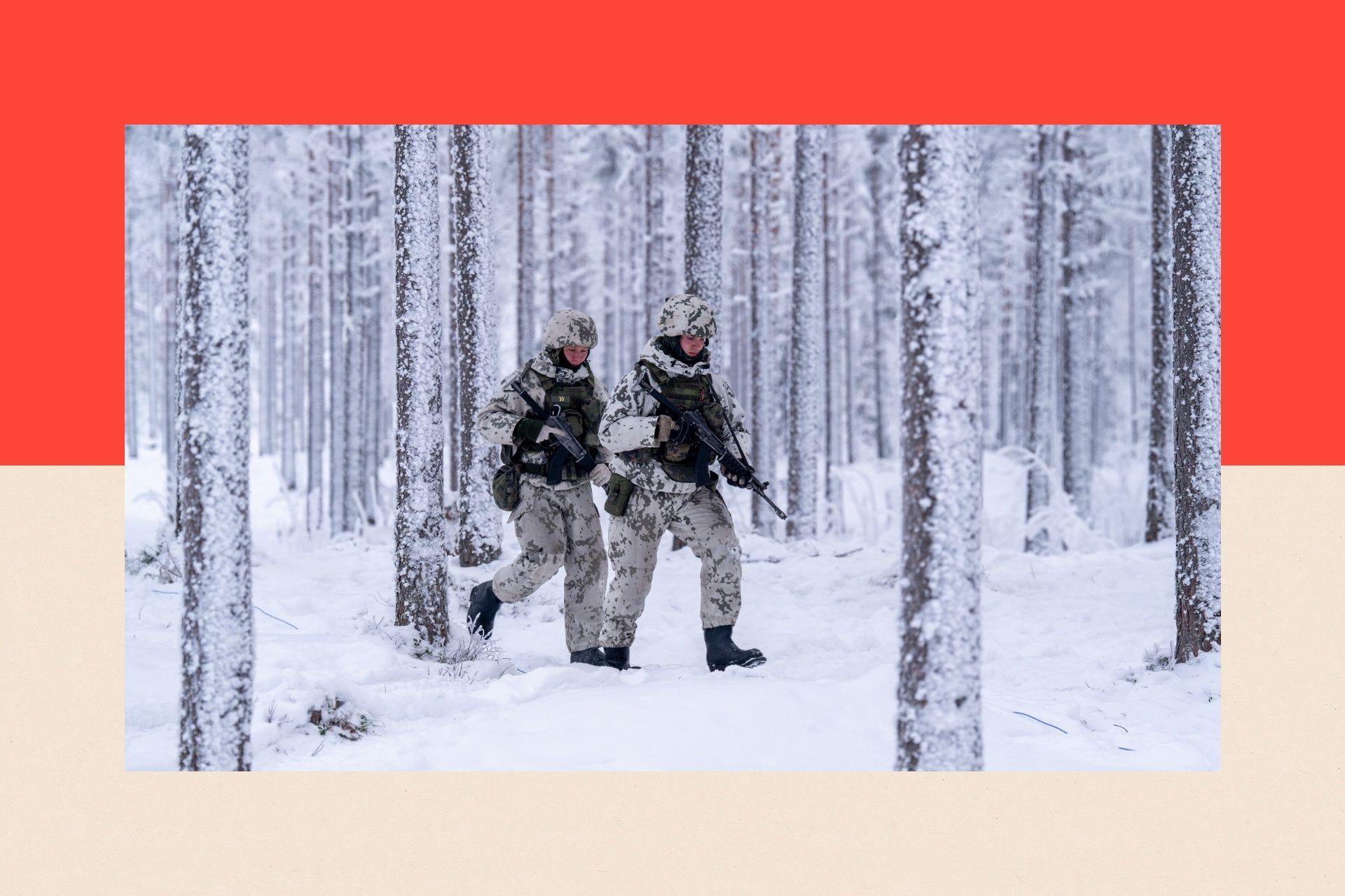Finnish conscripts wearing winter camouflage uniforms, armed with machine guns walk through the snow covered forest