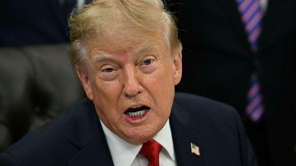 Donald Trump sits on a leather chair as he speaks in the Oval Office.
