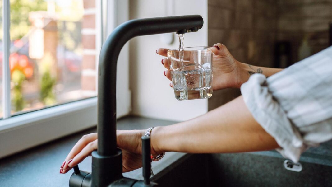 Complaints to watchdog about water firms jump 84% Hands only image of someone turning on a mixer tap to fill a glass of water