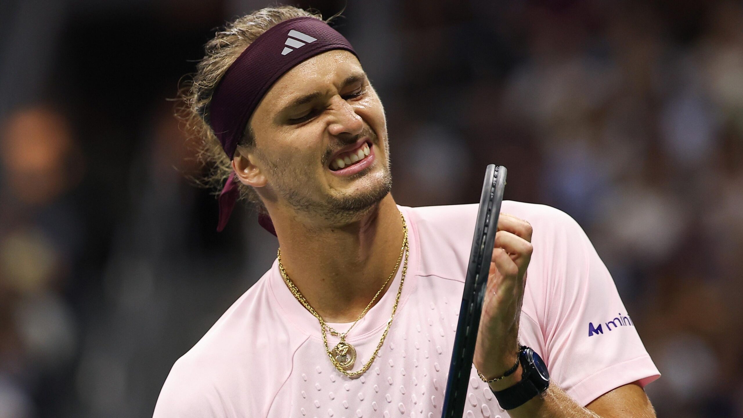 Alexander Zverev, wearing a light pink shirt and with gold jewellery around his neck, grimaces while holding his racquet during his second-round win over Quentin Halys at the US Open