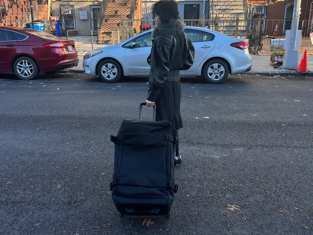 Image may contain: Adult, Person, Car, Transportation, Vehicle, Baggage, Machine, Wheel, Pedestrian, Clothing, and Coat