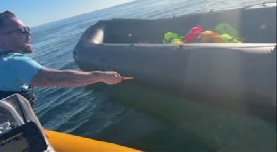 Anti-migrant campaigner leaning out of a boat appearing to hold a knife and to be shouting