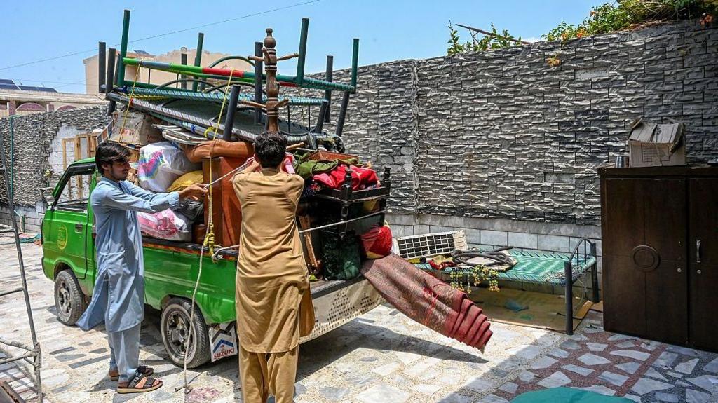 Afghan refugees load their belongings onto a small green truck in Peshawar on July 13, 2026, as they prepare to depart for Afghanistan.