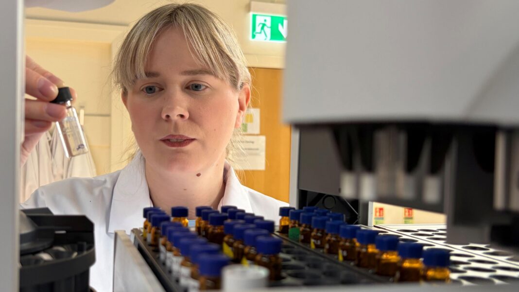 The deadly new drugs reshaping Scotland’s fight against addiction Close-up of a laboratory scientist placing a sample vial into an automated testing machine, with rows of specimen bottles in the foreground.