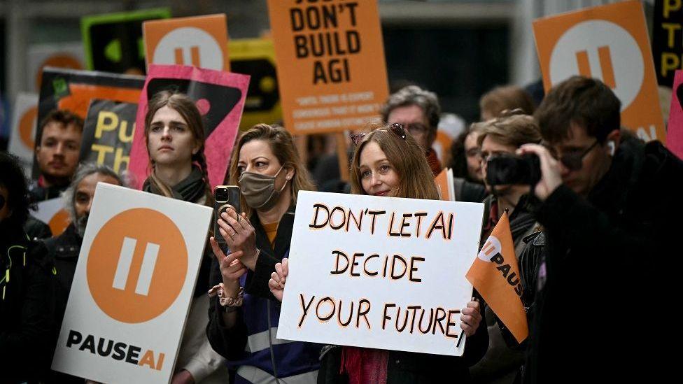 Protesters with orange banners and placards gather outside the offices of Google Deepmind at a protest organised by PauseAI UK.