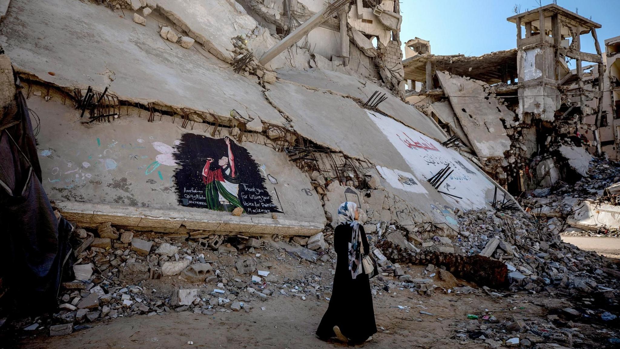 A woman passes a mural depicting US rapper Macklemore on the ruin of a war-damaged building in Gaza City (19 September 2026)