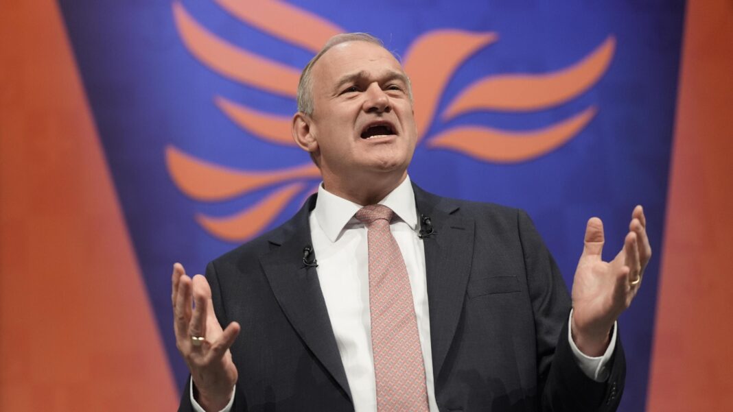 Sir Ed Davey at the Liberal Democrat party conference. He is pictured against a blue and red background, and he is gesturing with his hands as he makes his speech.
