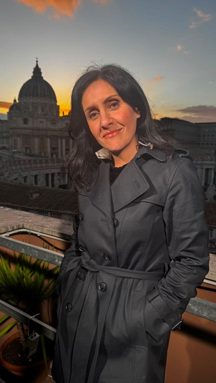 Maryam Moshiri stand in a black coat. The Vatican is in the background