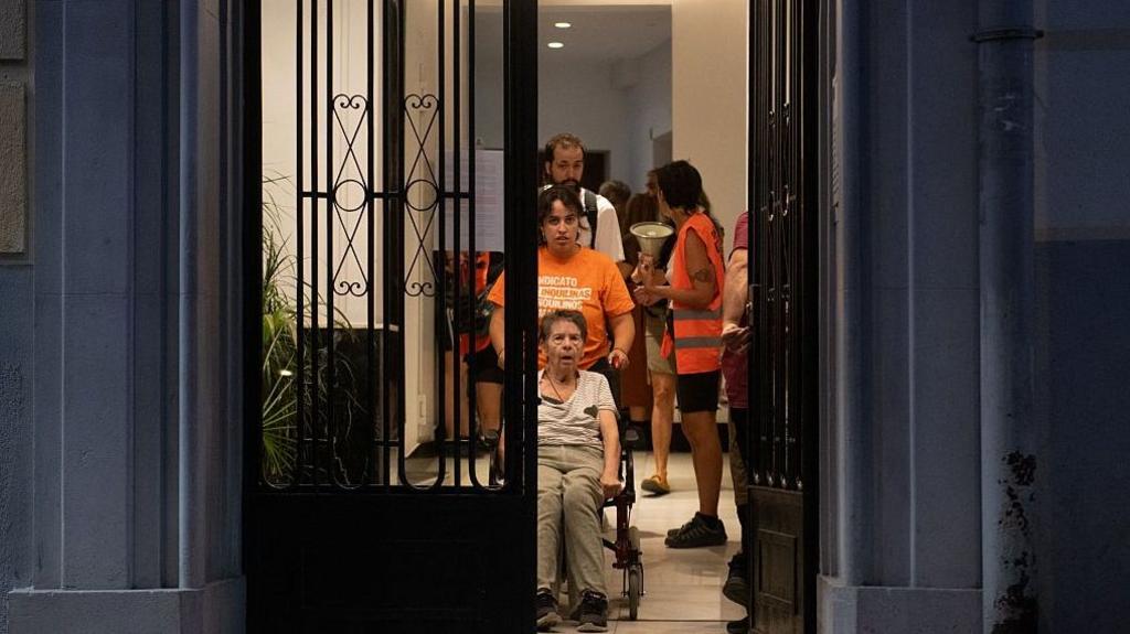 Maricarmen, in a wheelchair, is helped out of her house by supporters