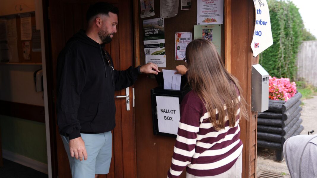 Villagers vote on independence over asylum plans A man in a black hoodie and a woman in a maroon and beige sweater cast their votes in Piddington.