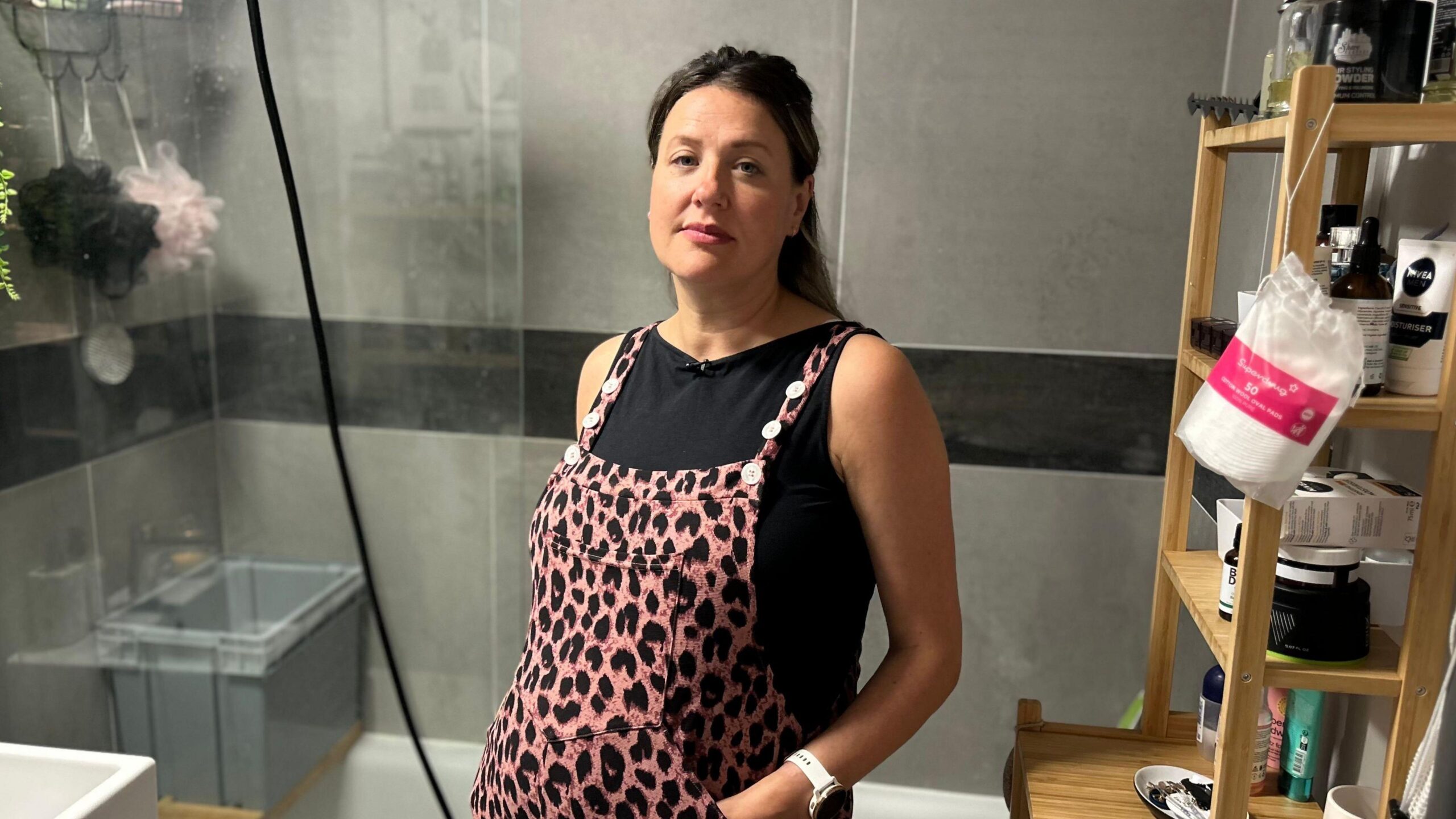 A pregnant Samantha Banner standing in a bathroom wearing pink leopard skin print dungarees over a black T-shirt