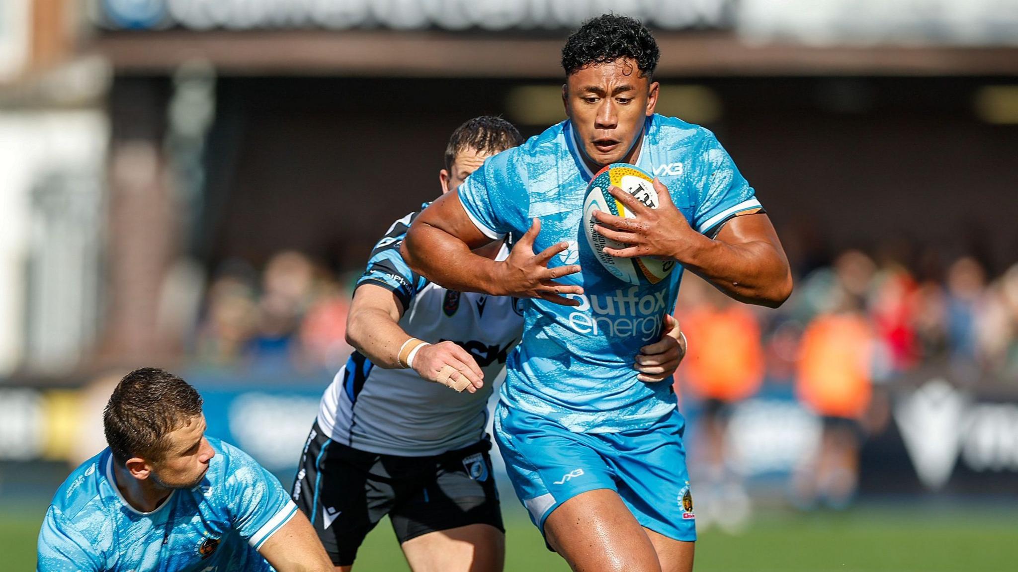 Greg Fisilau runs with the ball tucked under his left arm as a player tries to tackle him from behind, during a Prem Rugby Cup match for Exeter