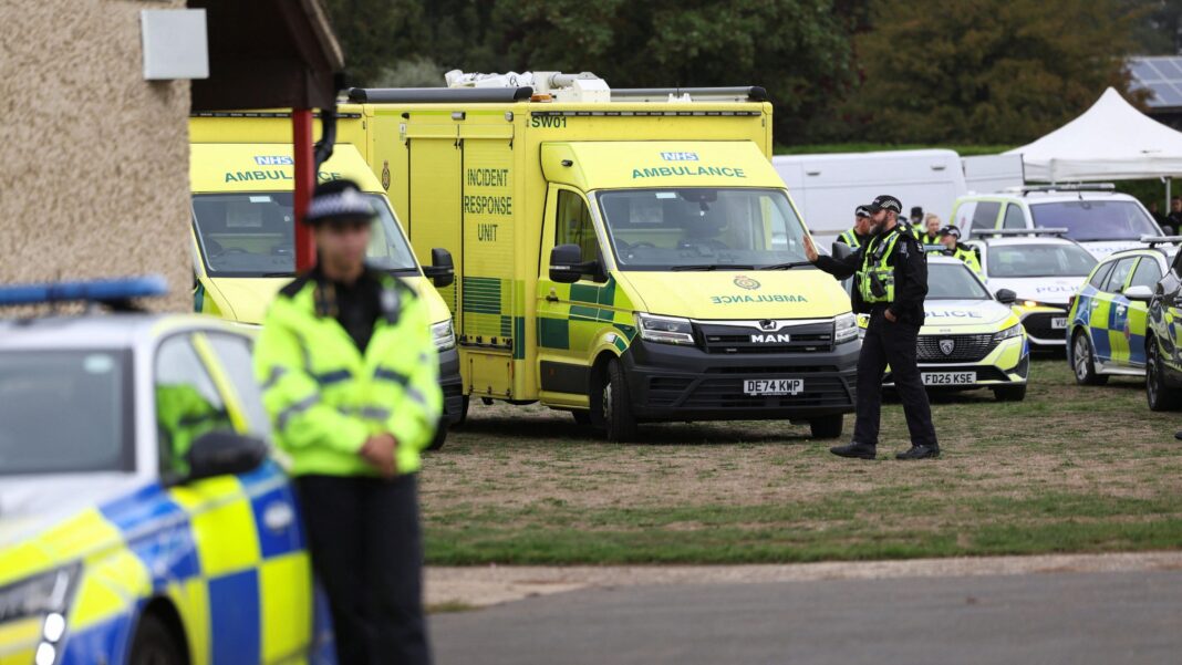Men arrested and houses evacuated in major incident near RAF Fairford A police officer is pictured leaning on a police car, with various emergency services in the background parked on grass.