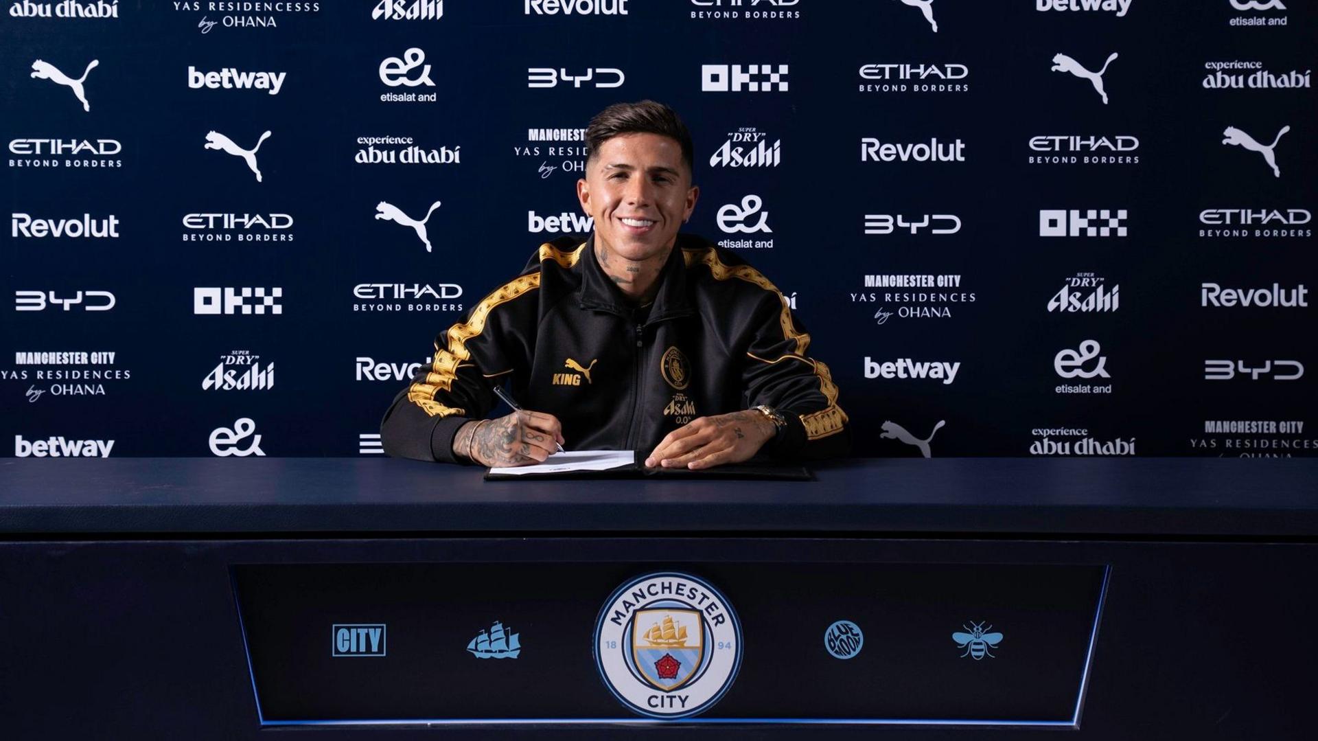 Enzo Fernandez sitting at a desk with a pen in his hand poised to sign a contract
