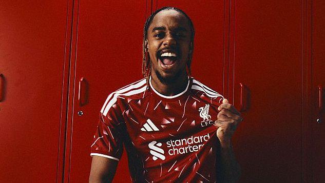 Bradley Barcola tugging on his Liverpool shirt badge with a smile on his face as he celebrates joining Liverpool