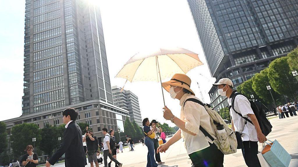 People walk in central Tokyo under the glaring sun of a summer heatwave, with one man protecting himself from the heat using a parasol