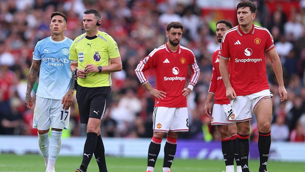 Players of Manchester City and Manchester United stand around as a VAR review is carried out