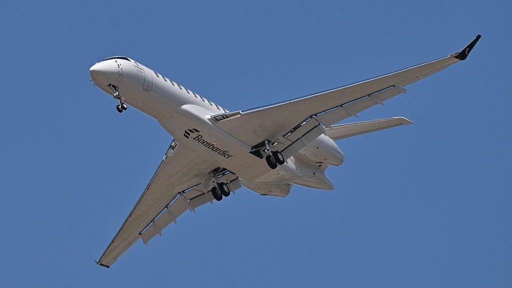 An image showing a Bombardier Global 8000 flying, with its bottom visible, showing its wheels and a Bombardier logo.
