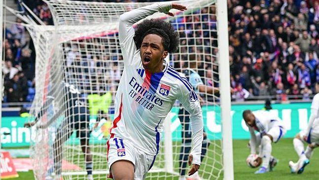Malick Fofana, wearing Lyon's white kit with a red-and-blue stripe, celebrates scoring a goal by waving his right arm in the air