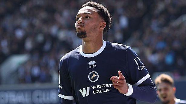 Femi Azeez, wearing Millwall's dark blue home kit, points to some fans during a goal celebration