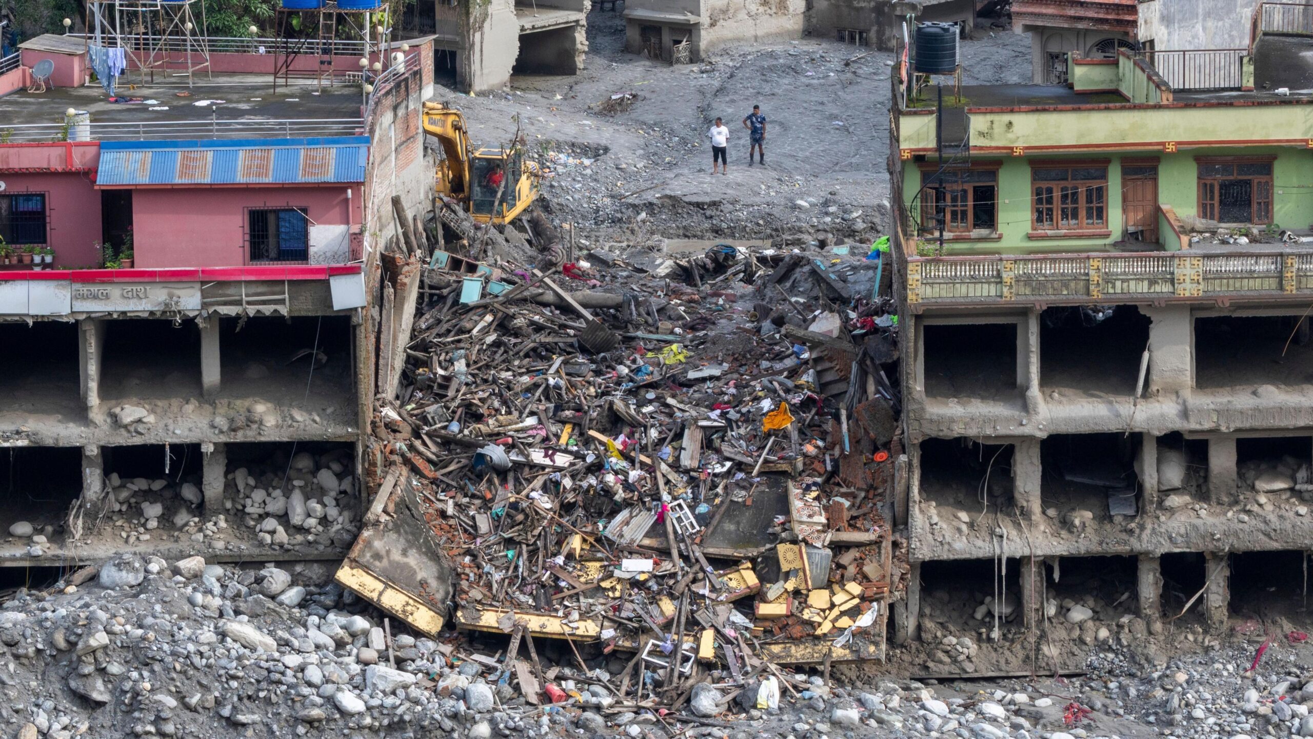 A building has totally collapsed, and is seen between two damaged, but still standing buildings.