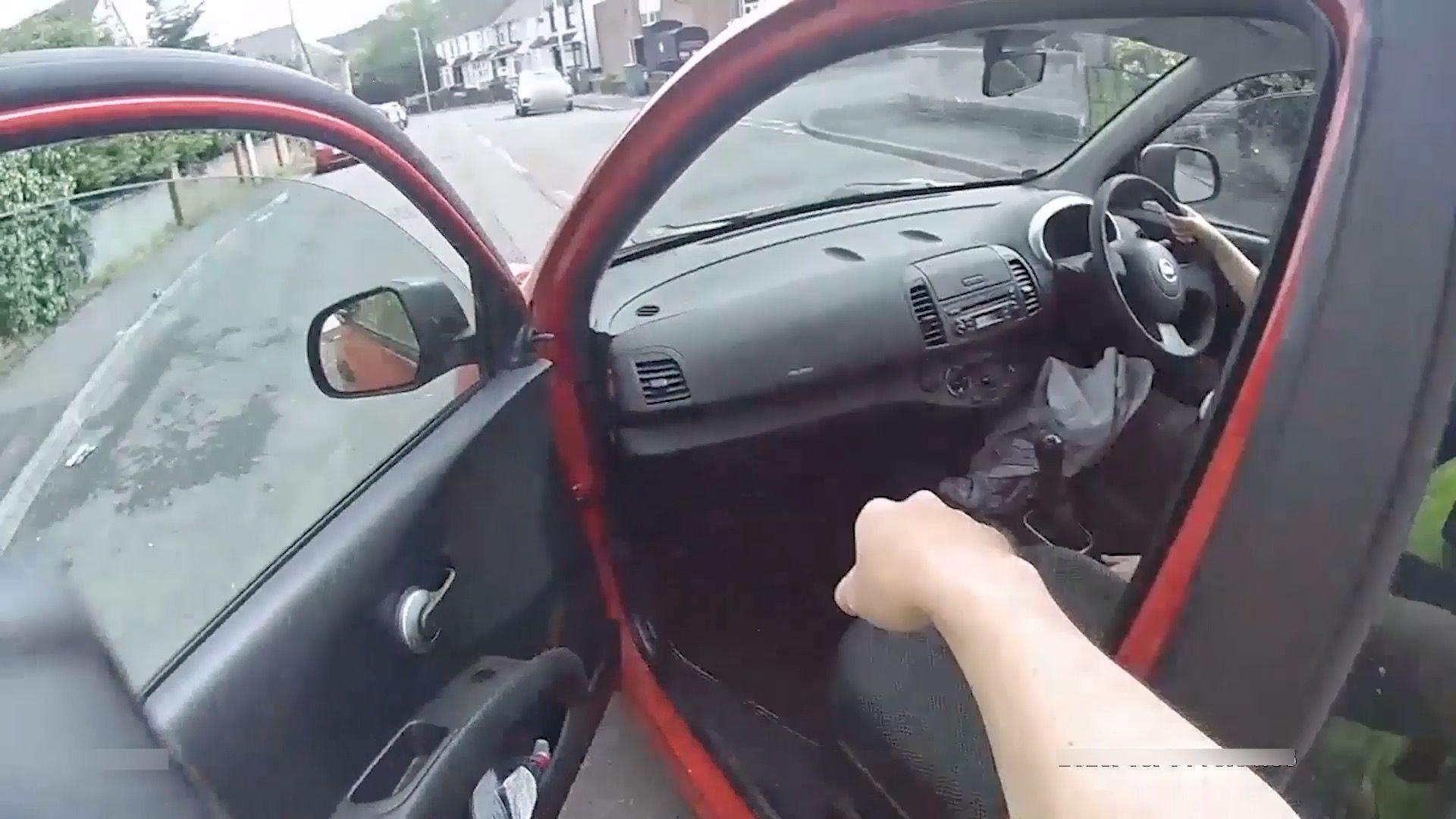 A screenshot from a video, showing the perspective of a camera worn by a person getting into a red car.