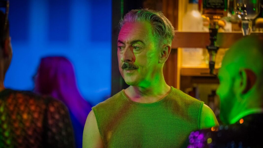 Drag Race co-creator fears for queer representation after BBC drops show Actor Alan Cumming is in a night club, he's looking worried and is looking away to the left of the camera. The lighting in the bar is green and you can see bottles of alcohol in the background.