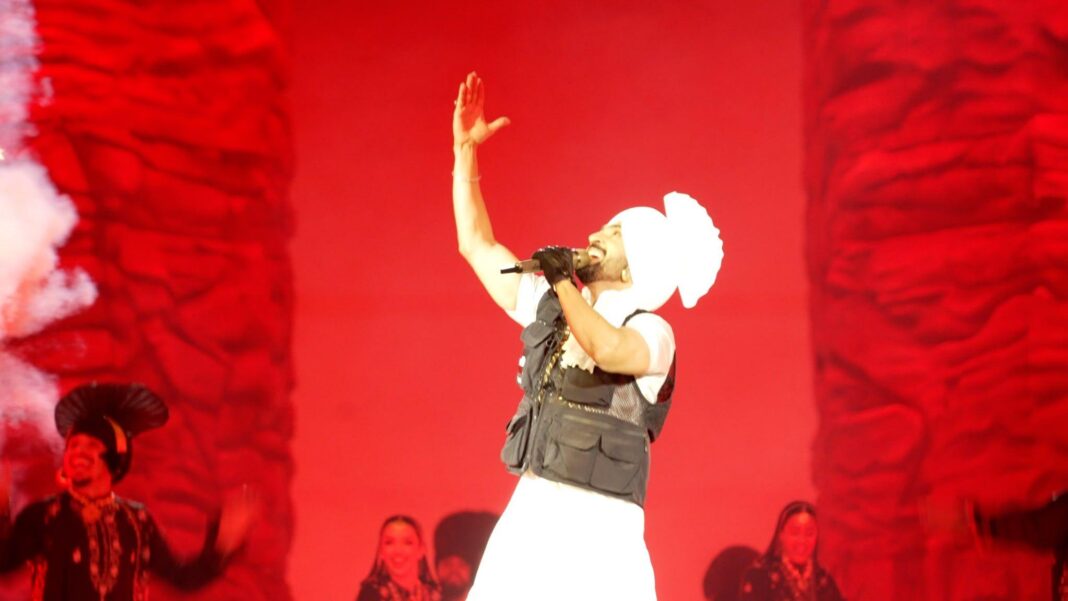 Diljit Dosanjh performing at Wembley Stadium against a red backdrop