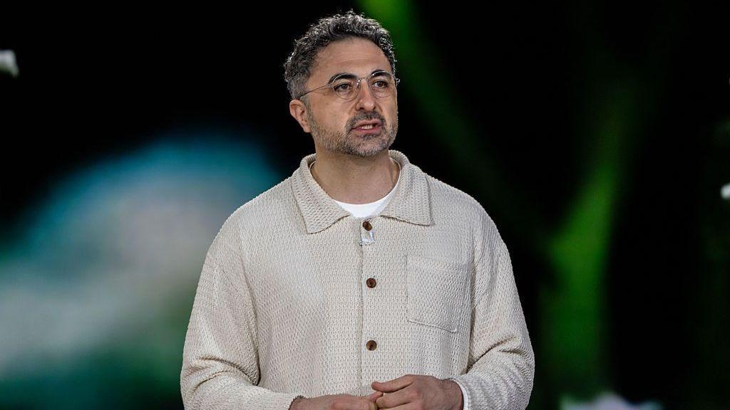 Microsoft's head of AI, Mustafa Suleyman, on stage and wearing a cream top with a collar and a white t-shirt.