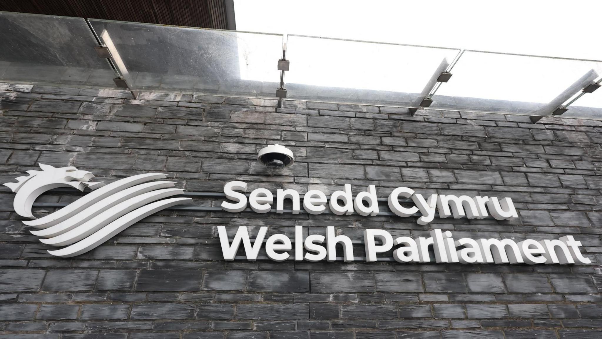 A sign with with letters on a black stone background saying SENEDD CYMRU WELSH PARLIAMENT