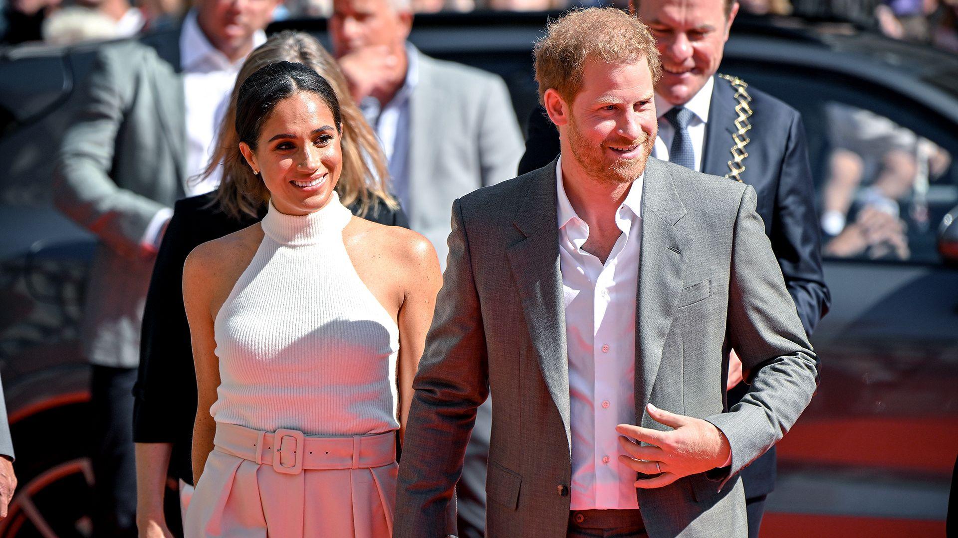 Meghan and Harry look to the right of frame while walking in front of a car and a crowd of people while arriving at the Invictus Games in Dusseldork in 2022.