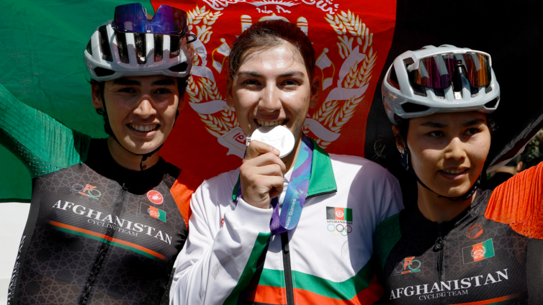 Cyclist who dressed as man to avoid Taliban wins silver medal Fariba Hashimi pretends to bite her medal after winning the Aichi-Nagoya Asian Games women's cycling road race silver in Shinshiro, as she stands between two Afghanistan fellow riders