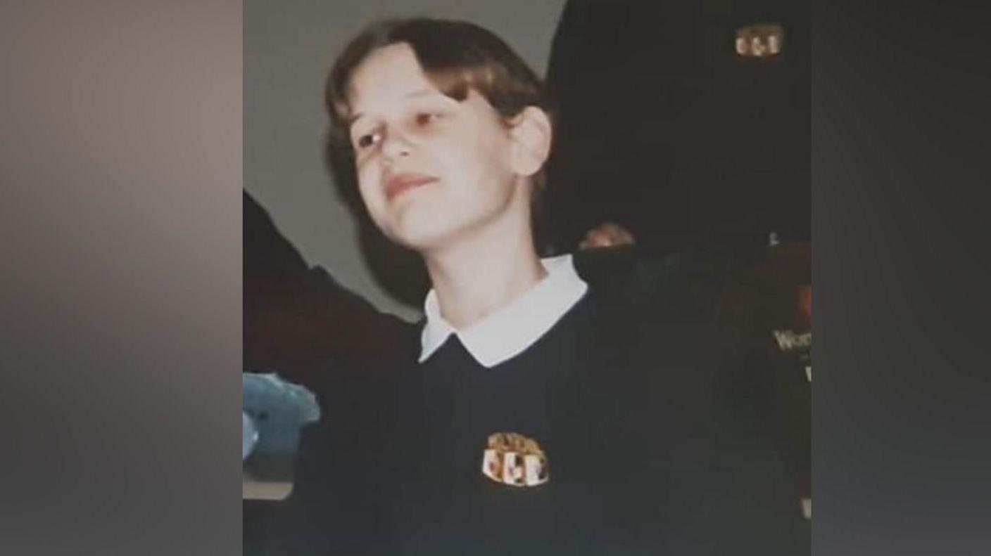 A boy wearing a navy blue school uniform, looking just past the camera. He's sitting at a desk. In front of him is a Pepsi-can-style pencil case.