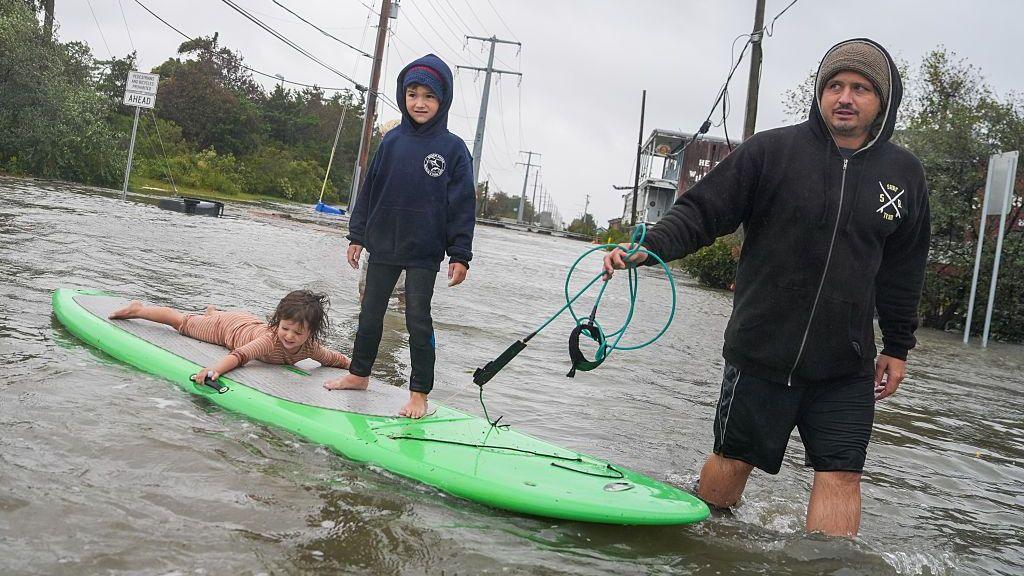 A resident pulls a paddle board carrying his children down a flooded road during a nor'easter storm.