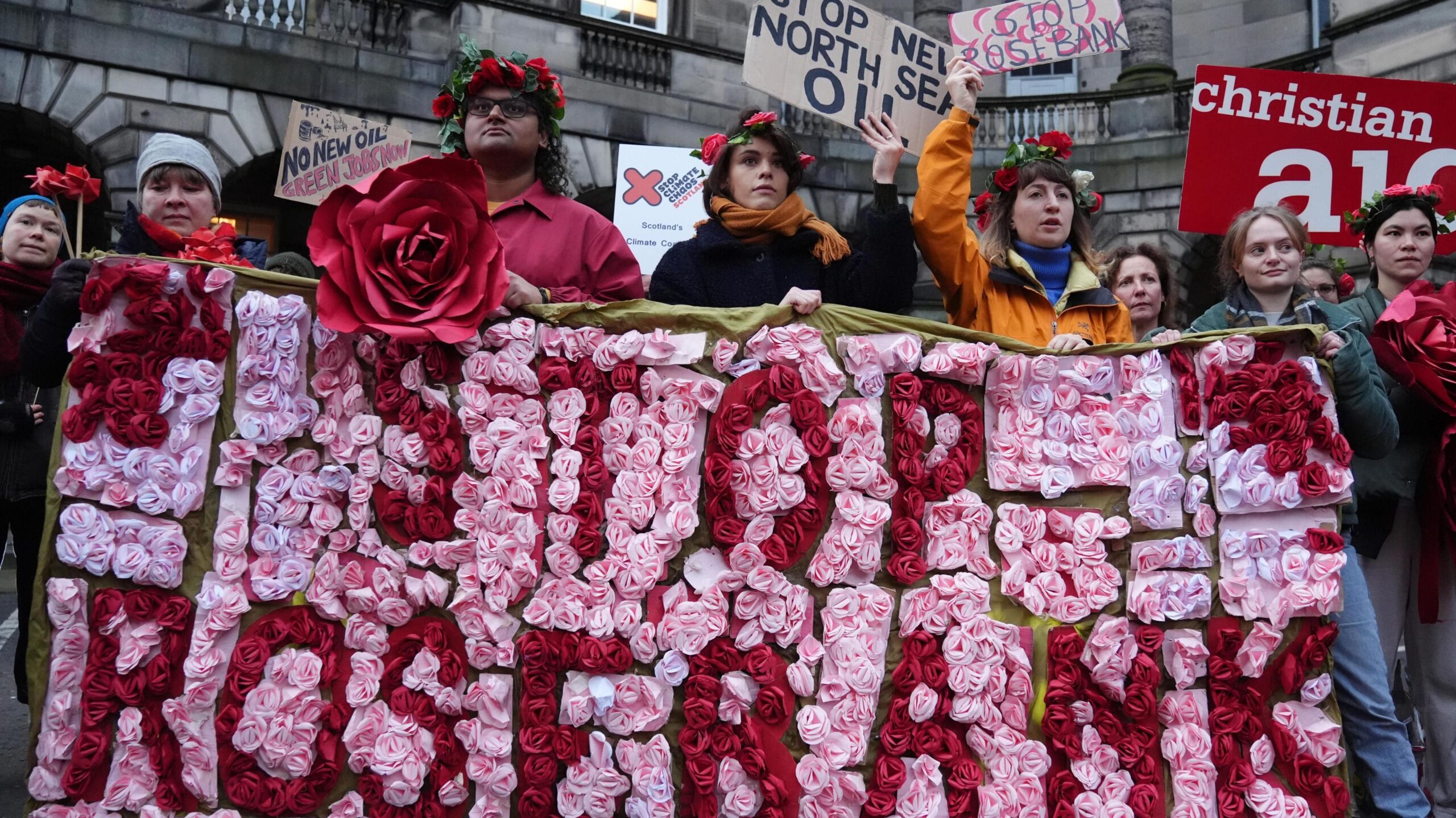 Climate activists from Greenpeace and Uplift during a demonstration outside the Scottish Court of Session, Edinburgh, on the first day of the Rosebank and Jackdaw judicial review hearing. They are holding a Rosebank banner made of red and pink flowers and waving "Stop New North Sea Oil" banners.