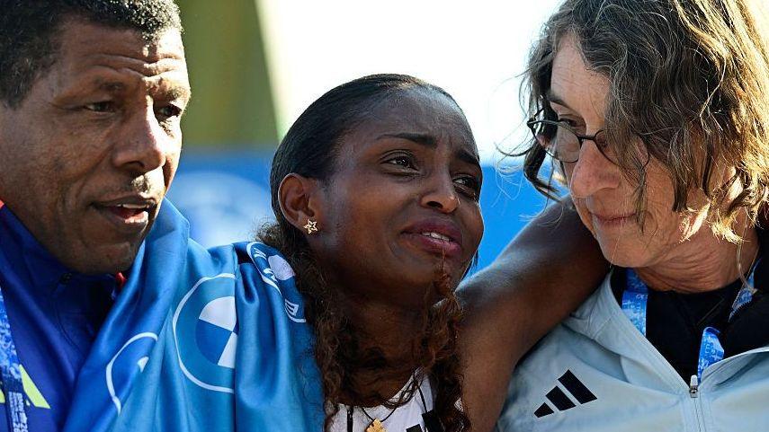 Ethiopia's Tigst Assefa (C) is helped off the track after crossing the finish line to win the women's race of 52nd Berlin Marathon in Berlin, Germany on September 27, 2026.