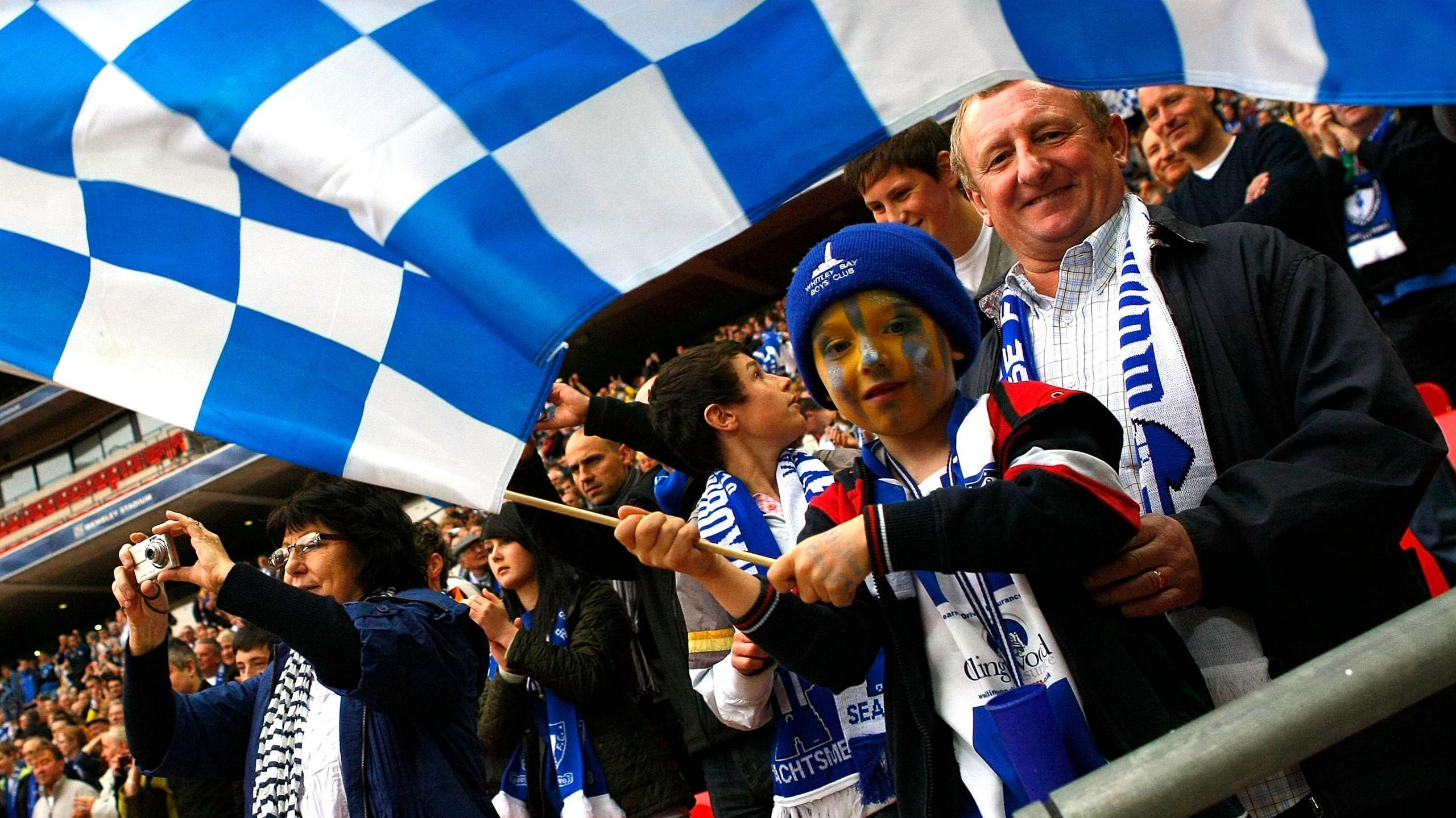 Whitley Bay fans wearing the club's blue and white colours and waving a flag