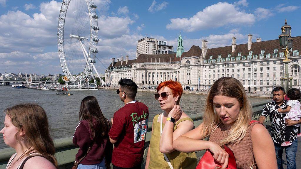 Tourists walking across Westminster Bridge in London with the London Eye in the background