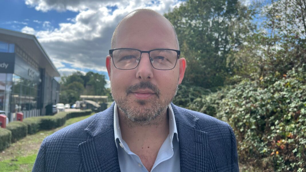 Group entered hotel where Pakistani cricketers mistaken for migrants were staying George Madgwick looks into the lens of the camera. He has a full, short, grey beard and black-rimmed glasses. He is wearing a light blue, open-collar shirt and a navy blue tweed jacket.