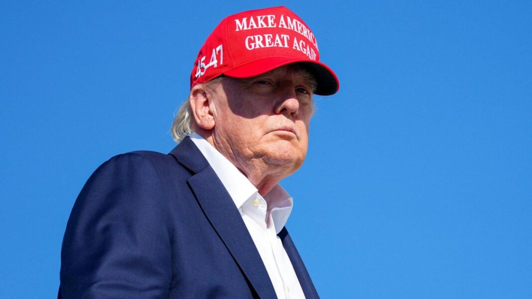 Iceland summons US ambassador over Trump’s stars and stripes map US President Donald Trump wears a blue suit jacket, white shirt and red cap, embazoned with the phrase MAKE AMERICA GREAT AGAIN in white writing. The sky is a deep blue behind him.