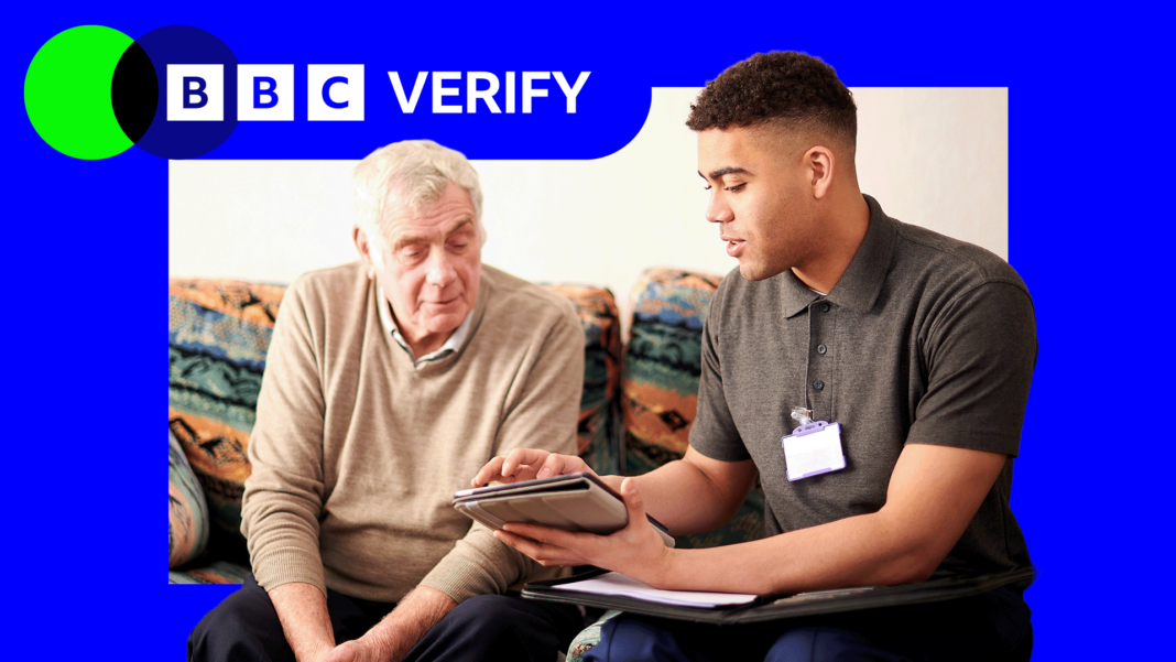 A senior man sat down speaking to a younger adult wearing a lanyard and holding a tablet.