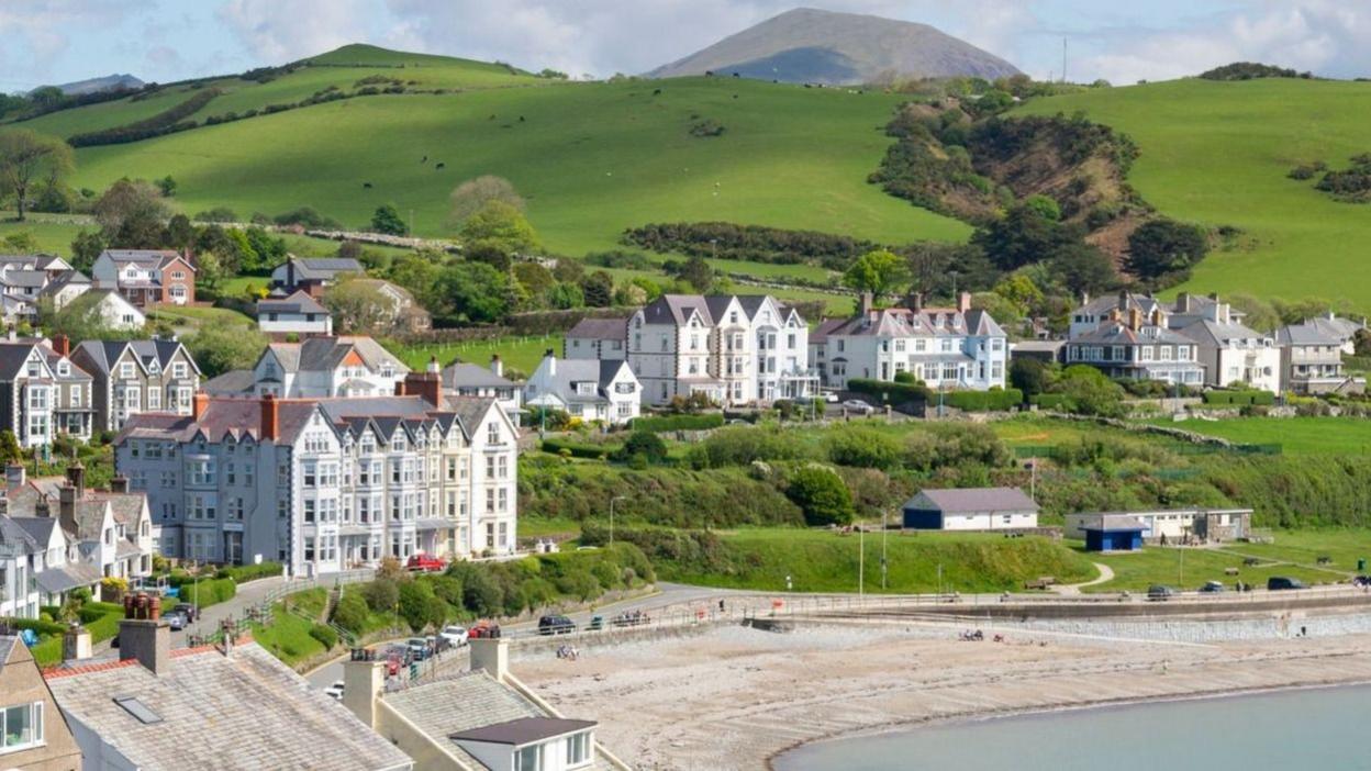 General view of the seaside town of Criccieth in north Wales, including a pebble beach and large townhouses overlooking the seafront, in the sunshine.
