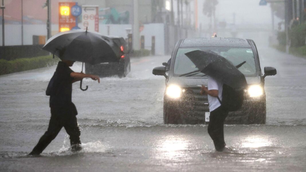 Two men with umbrellas are ankle-deep in water as they cross a road in Funabashi, Chiba Prefecture, Japan