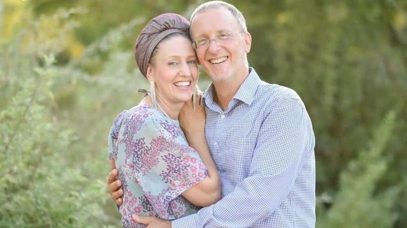 A man and a woman hug. They are smiling at the camera.