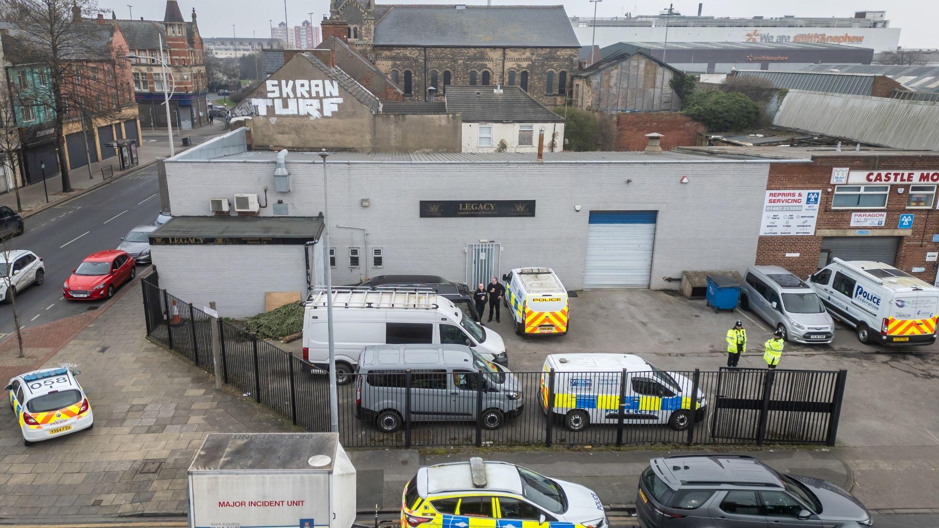 Aerial view of the Legacy funeral home in Hull a grey industrial unit with a number of police cars and officers in the car park