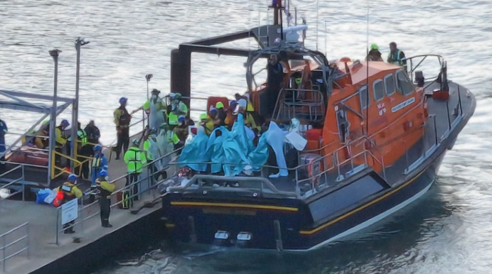 People wrapped in blankets on the back of an RNLI lifeboat moored by a pontoon at Eastney, Portsmouth, on 6.9.26