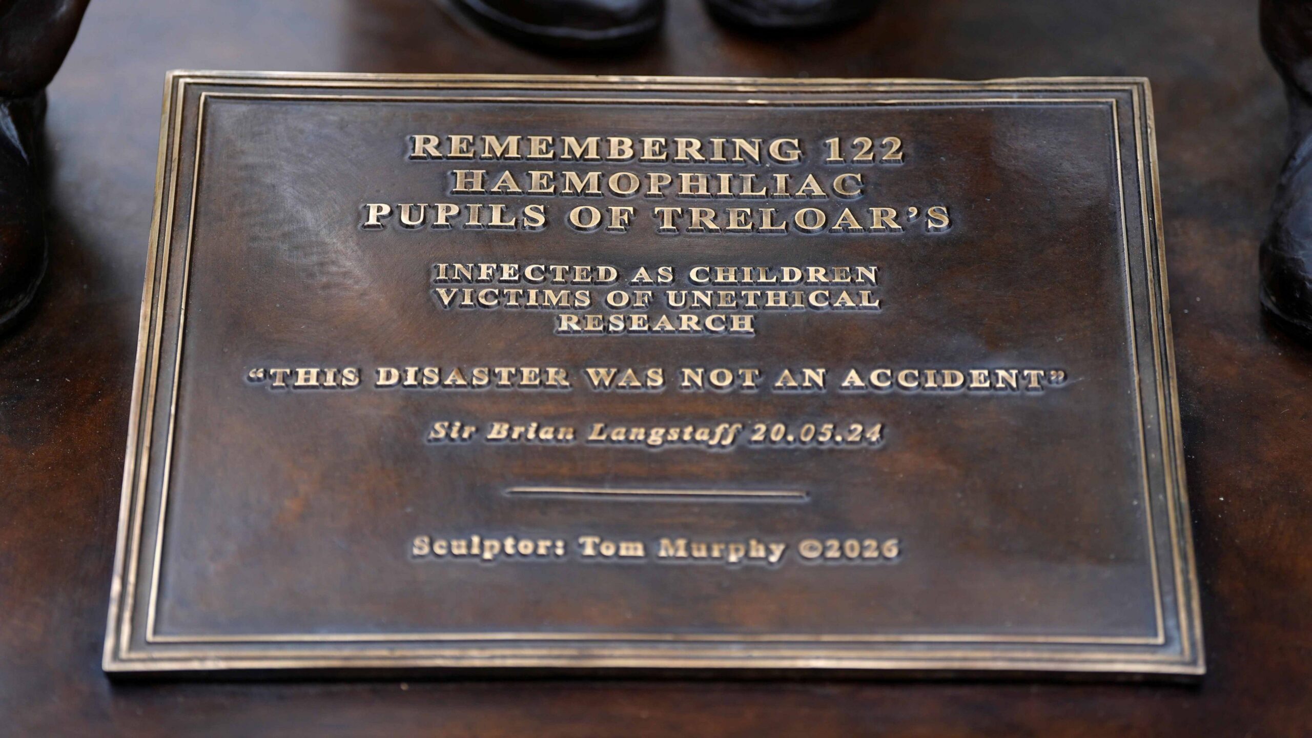 The bronze plaque reads: Remembering 122 haemophiliac pupils of Treloar's. Infected as children, victims of unethical research. "This disaster was not an accident." Sir Brian Langstaff 20.05.24. Sculptor Tom Murphy 2026.